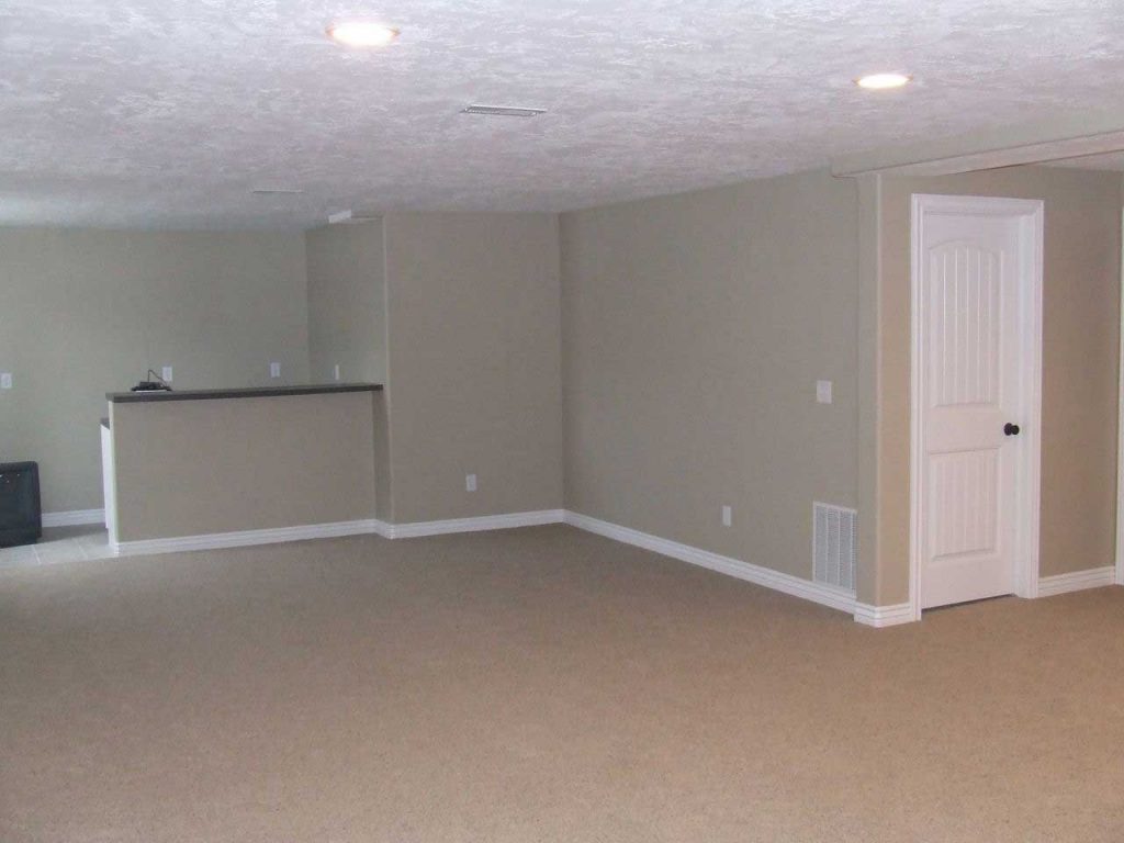 An empty room with walls painted in a light brown cream color. A white door is closed, adding a contrast to the wall color. The room appears clean and well-maintained, ready for use or decoration